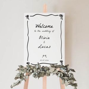 May include: White wedding welcome sign with black calligraphy. The sign reads "Welcome to the wedding of Olivia & Lucas 04.05.2026".