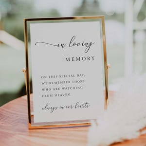 May include: A gold-framed sign with the words "in loving memory" and a heartfelt message. The sign is displayed on a wooden surface, suitable for memorial events or celebrations of life.