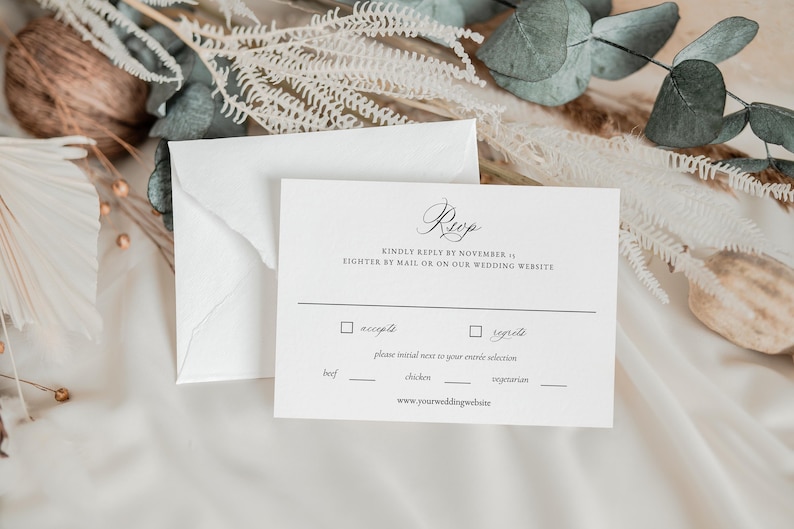 May include: A white RSVP card with black text. The text reads "Rup" in cursive, "Kindly reply by November 1st, either by mail or on our wedding website."  The card has two checkboxes, "accept" and "regret."  The card also has a section for meal selection with the options "beef", "chicken", and "vegetarian". The card ends with the website address "www.yourweddingwebsite".