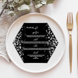 May include: A black and white hexagonal menu card with a silver glitter background. The menu card lists appetizers, salad, entree, and dessert options. The text "menu" is written in cursive at the top of the card.