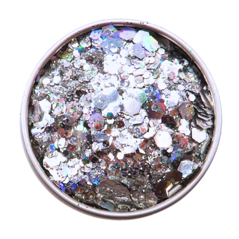 May include: A round container filled with silver glitter. The glitter pieces are various shapes and sizes, reflecting light with a shimmering effect. The container has a silver rim and is set against a white background.