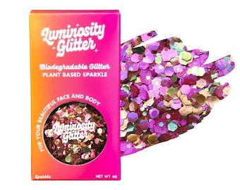 May include: A box of Luminosity Glitter in a gradient pink and orange box with the text "Biodegradable Glitter" and "Plant Based Sparkle". A swatch of multi-colored glitter is next to the box. The glitter is for face and body use.