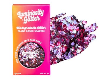 May include: A rectangular box of Luminosity Glitter with a pink and orange gradient. The text reads Luminosity Glitter, Biodegradable Glitter, Plant Based Sparkle, For Your Beautiful Face And Body, Sparkle, and Net Wt 6g. A pile of pink glitter sits beside.