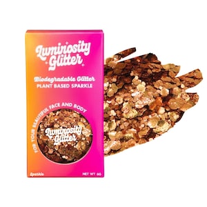 May include: A box of Luminosity Glitter in a pink and orange gradient. The box features the text "Biodegradable Glitter" and "Plant Based Sparkle." A circular window displays the glitter, with a loose pile of glitter to the right. The glitter is a mix of gold and bronze tones.