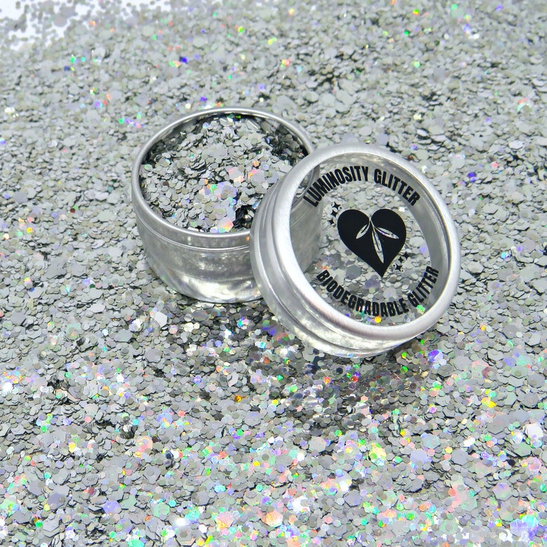 May include: A silver glitter in a small tin container. The container has a black label that reads "Luminosity Glitter Biodegradable Glitter".