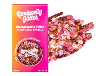 May include: A box of Luminosity Glitter in a gradient orange and pink color scheme, with the words "Luminosity Glitter" and "Biodegradable Glitter" printed on the front. A sample of the glitter is displayed next to the box. The glitter is a mix of pink, gold, and iridescent colors.