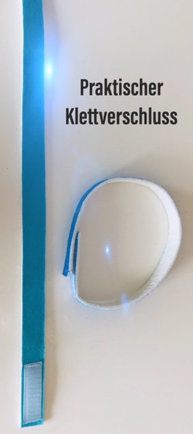 May include: A blue and white hook and loop fastener, with the text "Praktischer Klettverschluss". The fastener is made of a soft, textured material. The image shows a long strip and a circular band.
