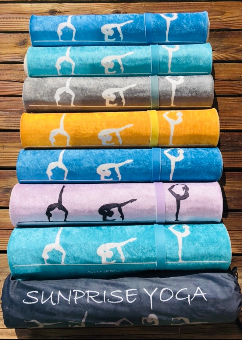 May include: Rolled yoga mats in various colors, including blue, gray, yellow, and purple, each featuring a white yoga pose design. The mats are secured with matching straps. A dark gray bag with "SUNPRISE YOGA" is at the bottom.