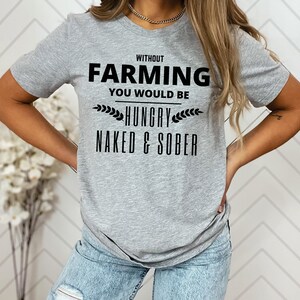 Puede incluir: Una camiseta gris con el texto negro: "WITHOUT FARMING YOU WOULD BE HUNGRY NAKED & SOBER". La camiseta tiene cuello redondo y mangas cortas. El texto está centrado en la parte delantera de la camiseta.