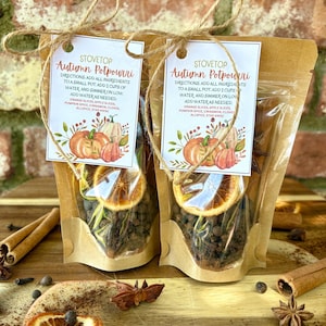 May include: Two clear cellophane bags filled with autumn potpourri ingredients, each tied with twine and a tag. The tags read "Stovetop Autumn Potpourri" and include instructions and a list of ingredients like orange slices and cinnamon.
