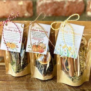 May include: Three clear cellophane bags filled with potpourri, each with a decorative tag. The tags read "Christmas Potpourri", "Autumn Potpourri", and "Spring Potpourri". The bags are tied with twine and contain dried fruit, spices, and herbs.