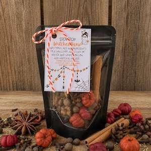 May include: A black pouch containing a stovetop witches brew mix with a white tag tied by orange and white twine. The tag features a ghost illustration and instructions for simmering orange slices, cinnamon, cloves, allspice, star anise, and mini dried pumpkins.