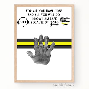 Op de afbeelding: Ingelijste print met de tekst "FOR ALL YOU HAVE DONE AND ALL YOU WILL DO I KNOW I AM SAFE BECAUSE OF you." Bevat een handafdruk, een 911-symbool en een hart met een dunne gele lijn.