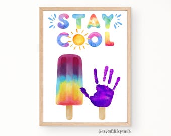 May include: Watercolor print in a wooden frame featuring the words "STAY COOL" above a colorful popsicle and a purple handprint. The popsicle is a gradient of purple, blue, yellow, and orange. The sun is yellow.