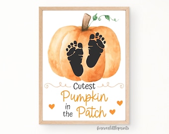 May include: A framed print showing a watercolour pumpkin with two black footprints. The text reads "Cutest Pumpkin in the Patch" in orange script, with orange heart accents. The print has a light wood frame.