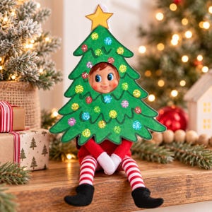 May include: A small elf doll wearing a red and white striped outfit with black shoes, positioned behind a green cardboard Christmas tree cutout. The tree features a yellow star at the top and colorful glittery circular ornaments.