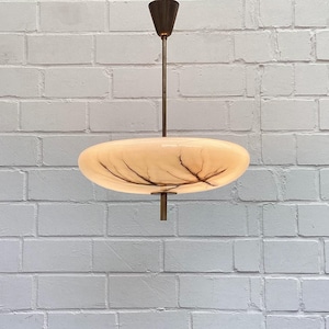 May include: A pendant light fixture featuring a flat, circular, cream-colored glass shade with dark, branch-like veining. The shade is suspended by a thin, dark metal rod connected to a matching conical ceiling canopy.