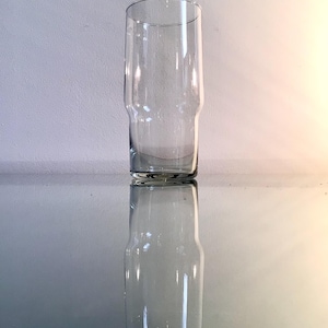 以下が含まれることがあります： わずかに広いベースとまっすぐな開口部を備えた透明な円筒形のグラス。 グラスは光沢のある表面に反射し、対称的な画像を作成します。 飲み物用。
