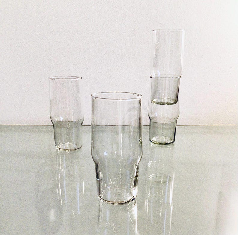 May include: Four clear glass drinking glasses, three stacked on top of each other. The glasses are tall and cylindrical with a slightly flared lip.