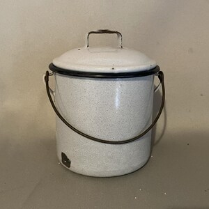 May include: White enamelware container with a black rim and a brown handle. The container has a lid with a brown handle.