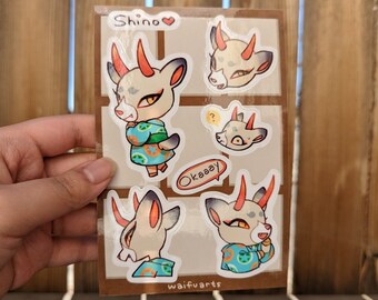 May include: A set of five stickers featuring a cartoon animal with horns, wearing a blue and orange patterned shirt. The stickers include different expressions and poses of the character. The text "Shino", "Okasay", and "waifuuarts" are included on the stickers.