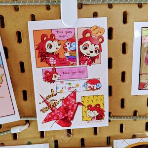 Könnte beinhalten: Ein Comic-Strip mit einem roten Fuchs-Charakter, der lernt, wie man einen Papierkranich faltet. Der Text im Comic lautet "This goes over and under... and voilà!" und "Now you try!"