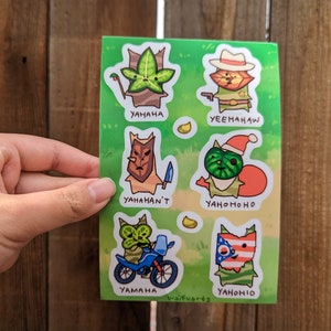 Puede incluir: Una hoja de seis pegatinas con personajes de dibujos animados en colores verde, rojo y marrón. Los personajes llevan sombreros y conducen una motocicleta. Las pegatinas tienen el texto "YAHAHA", "YEEHAHAW", "YAHAHAN'T", "YAHOMOHO", "YAHONIO" y "YAMAHA".
