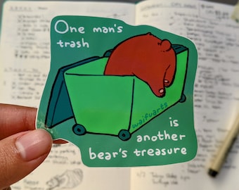 Op de afbeelding: Een groene prullenbak met wielen en een rode beer erin. De tekst op de sticker luidt "One man's trash is another bear's treasure" met de naam van de kunstenaar "waifuwarts" onderaan.