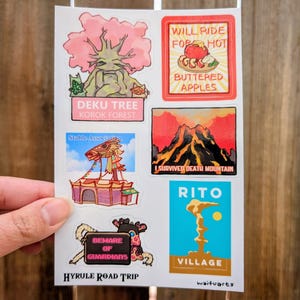 Puede incluir: Una hoja de pegatinas coloridas con ilustraciones y texto. Los diseños incluyen un árbol con follaje rosa, una montaña con lava y texto que dice "Will Ride For Hot Buttered Apples". Otro texto incluye "Deku Tree Korok Forest" y "Hyrule Road Trip".