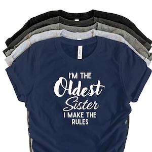 May include: A selection of t-shirts in shades of navy, grey, and black. The front navy blue tee features the white text: "I'M THE Oldest Sister I MAKE THE RULES".