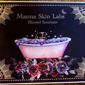 May include: A decorative card with the text "Manna Skin Labs Blessed Samhain" features a pink bathtub filled with purple bubbles. The card is framed with gold sunburst and floral accents, with a dark background.
