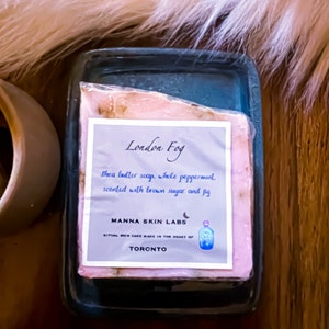 May include: A pink shea butter soap bar with a label that reads "London Fog" and "Shea butter soap, whole peppermint scented with brown sugar and fig". The label also includes the company name "MANNA SKIN LABS" and the city "TORONTO".