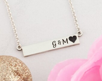 Könnte beinhalten: Silberne Bar-Halskette mit einem Herzen und der Inschrift "G & M".