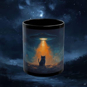 May include: Black coffee mug with a black cat silhouette looking up at a flying saucer with a beam of light shining down. The background is a dark blue night sky with stars.