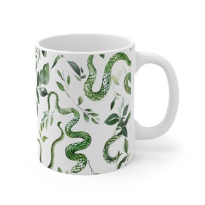 Könnte beinhalten: Weiße Keramiktasse mit einem Muster aus grünen Schlangen und Blättern. Das Muster wiederholt sich auf der gesamten Tasse.