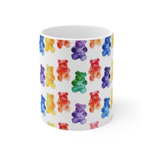 May include: White ceramic mug with a pattern of colorful gummy bear shaped like a bear. The bears are in a rainbow pattern of red, orange, yellow, green, blue, purple.
