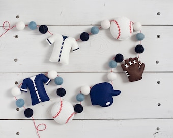 May include: A baseball-themed felt garland with white, blue, and brown felt balls, two baseballs, a baseball jersey, and a baseball glove.