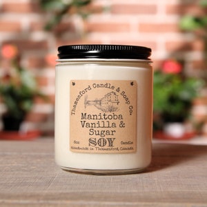 May include: An 8 oz soy candle in a clear glass jar with a black lid. The label is brown with white text that reads "Thamesford Candle & Soap Co." and "Manitoba Vanilla & Sugar SOY Candle Handmade in Thamesford, Canada".