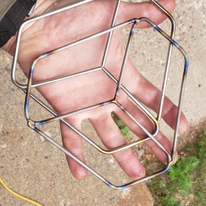 May include: Three interlocking metal rings, each with a square shape, are stacked on top of each other. The rings are made of a shiny metal with a rainbow-like iridescent finish.