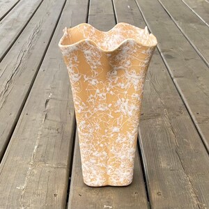 May include: A ceramic vase with a wavy rim and a white and yellow floral pattern.