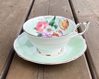 May include: A vintage teacup and saucer set with a floral design. The cup and saucer are both a pale green color with a gold trim. The floral design features pink, yellow, and white flowers.