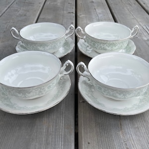 May include: Set of four white soup bowls with green floral designs and silver trim. Each bowl is paired with a matching saucer.