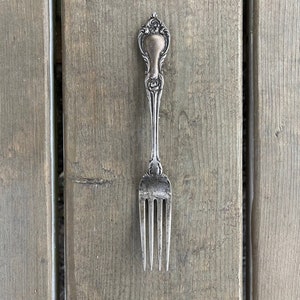 May include: A white ceramic mug with a black handle and the text "But First, Coffee" in a bold, black font. The mug is filled with a dark liquid, likely coffee, and sits on a light-colored surface.