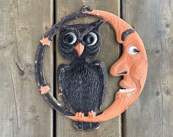 Può includere: Una decorazione di Halloween nera e arancione con un gufo e una luna crescente con un viso. Il gufo ha grandi occhi rotondi e un becco. La luna ha un viso sorridente con un naso storto.