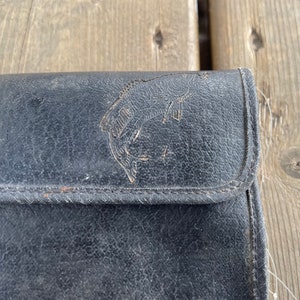 Puede incluir: Estuche de aparejos de pesca de cuero negro con un dise&ntilde;o de pez en relieve. El estuche tiene un cierre de bot&oacute;n a presi&oacute;n y bordes cosidos. El cuero muestra signos de desgaste, lo que le da un aspecto vintage. Un accesorio cl&aacute;sico para pescadores.