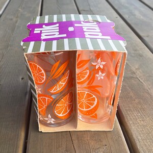 May include: A box of two orange juice glasses with an orange and flower design. The box is labeled "polk" in purple letters.