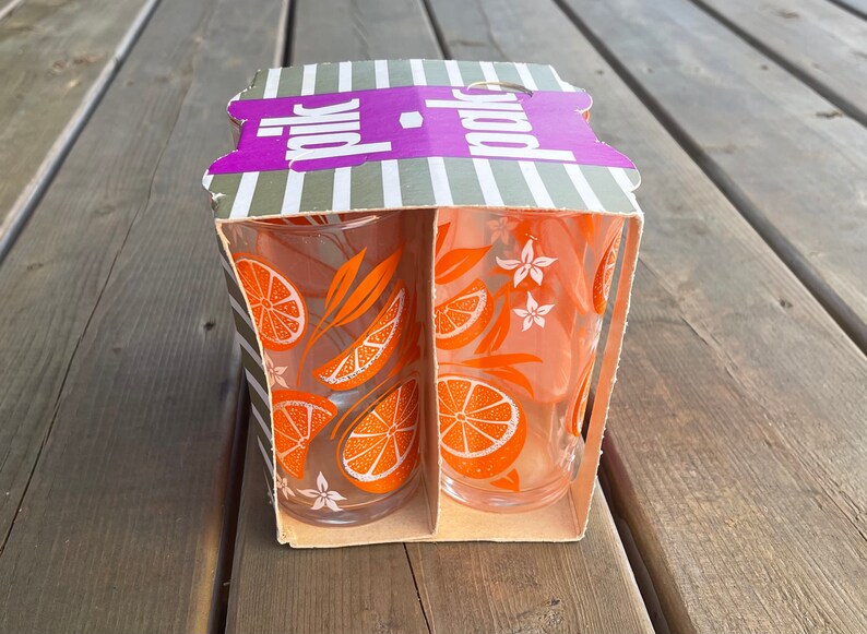 May include: A box of two orange juice glasses with an orange and flower design. The box is labeled "polk" in purple letters.