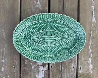 Può includere: Un piatto da portata ovale in ceramica verde caratterizzato da un motivo a intreccio di cesti al centro e un bordo decorativo con foglie in rilievo. La finitura lucida mette in risalto i dettagli complessi del design stampato.