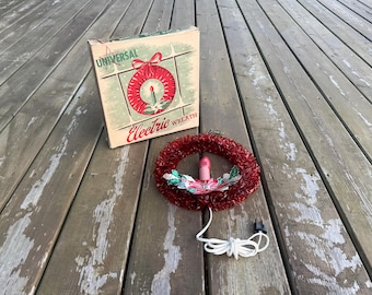 Può includere: Una ghirlanda elettrica vintage Universal con un anello di festone rosso, una lampadina rosa centrale e foglie di agrifoglio decorative. L'articolo include un cavo elettrico bianco con spina e viene fornito nella sua scatola di cartone originale.