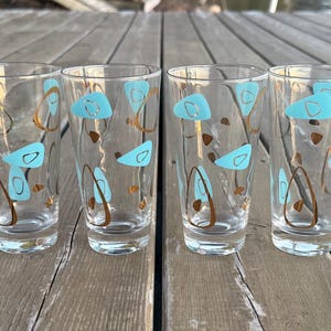 Peut inclure: Quatre verres à boire transparents avec un design moderne du milieu du siècle. Chaque verre présente un motif de formes bleu clair et de lignes courbes marron. Les verres sont cylindriques et reposent sur une surface en bois.